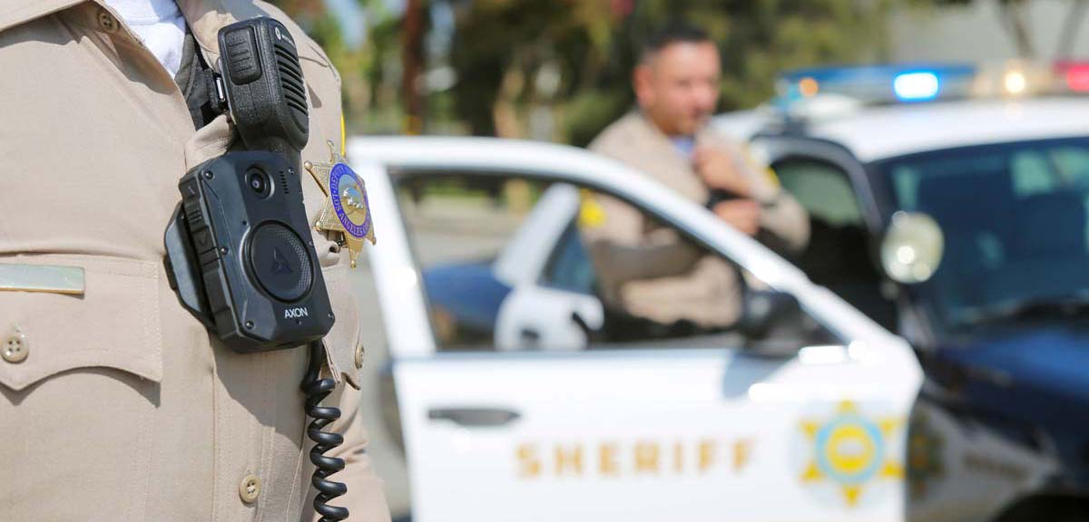 deputy wearing body worn camera standing in front of Patrol car