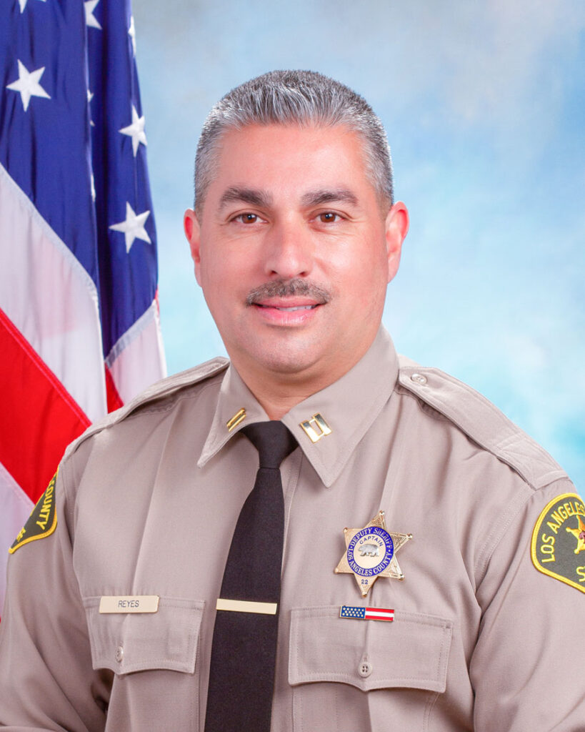 Portrait of Captain Mark Reyes in uniform, sitting infront of the American Flag