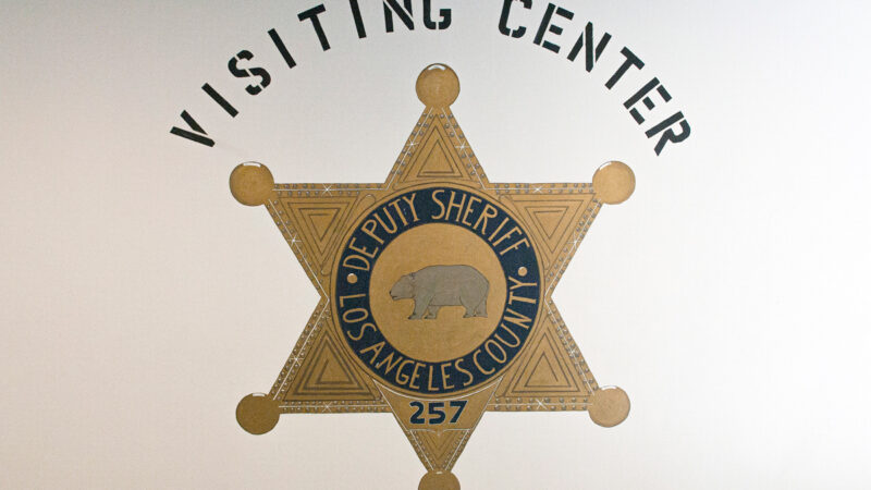 Picture of hand painted sheriff's badge, painted on a white wall in the C R D F Jail. The words above read, "Visiting Center".