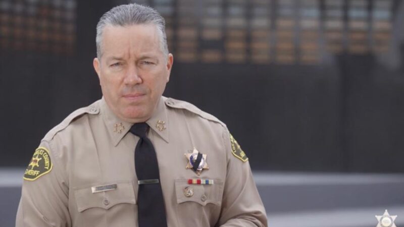 Picture of Sheriff Villanueva in uniform stading infront of the LASD Memorial Wall addressing the camera.