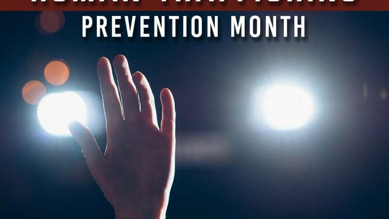 image of a person holding up thier hand calling for help .There are lights from an on comming car driving towards the viewer. Text accross the top reads National Human Trafficking prevention Month.